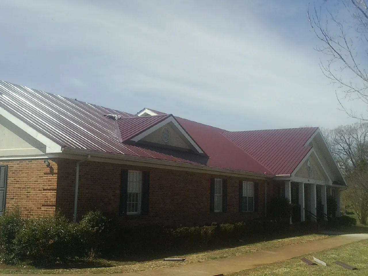 Red metal roof with gabled entries on a long brick building, from a Hail Damage Roof Repair job in Winchester