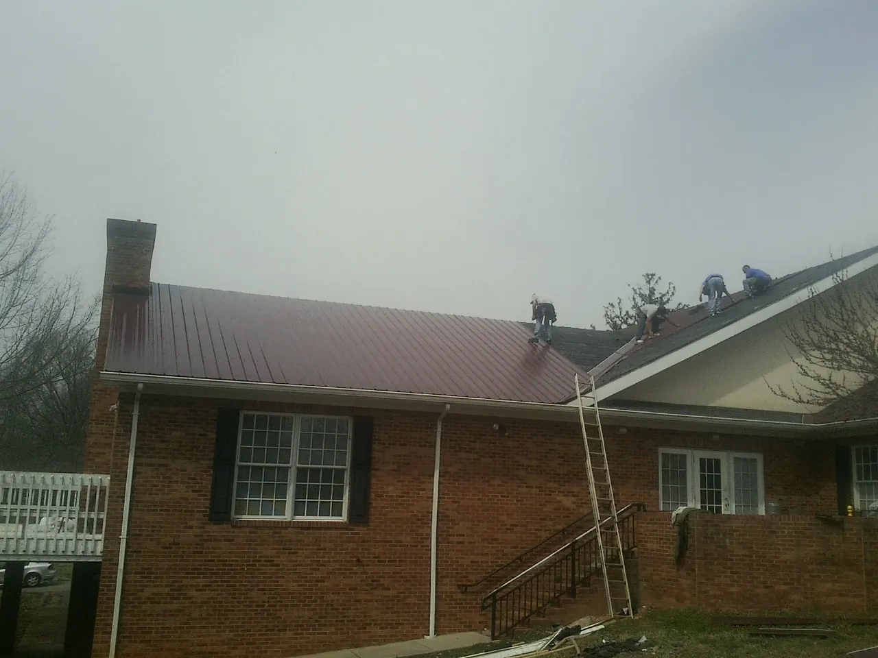 Crew setting red metal roofing panels on a brick home in Winchester